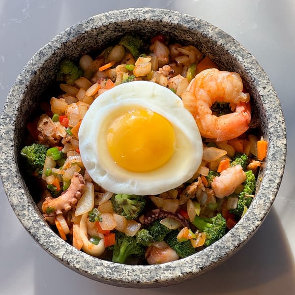 Korean seafood bibimbap with shrimp, octopus, vegetables, and a fried egg in a stone bowl.
