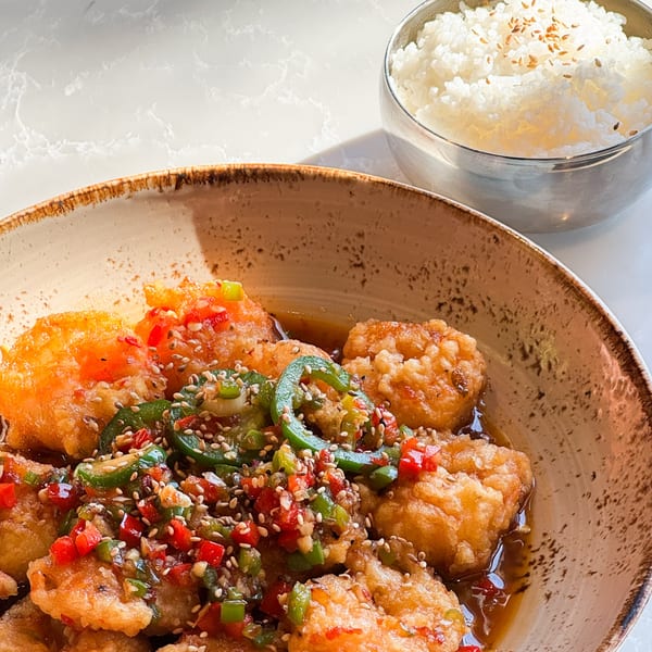 Crispy Korean fried chicken with red and green peppers, sesame seeds, and a side of white rice.