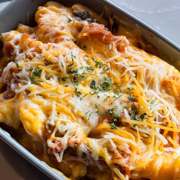 Close-up of a cheesy Korean dish, possibly tteokbokki, topped with melted cheese and herbs in a gray baking dish.