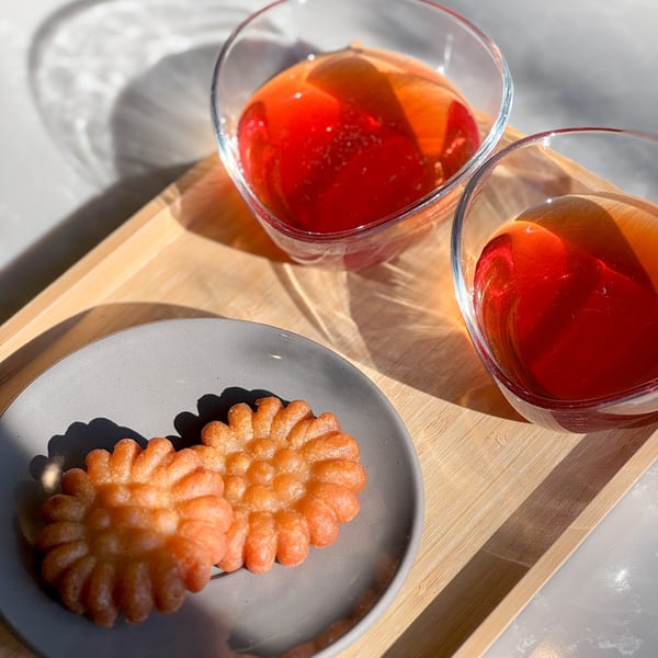 Two Korean yakgwa cookies on a grey plate next to two glasses of red sujeonggwa punch.