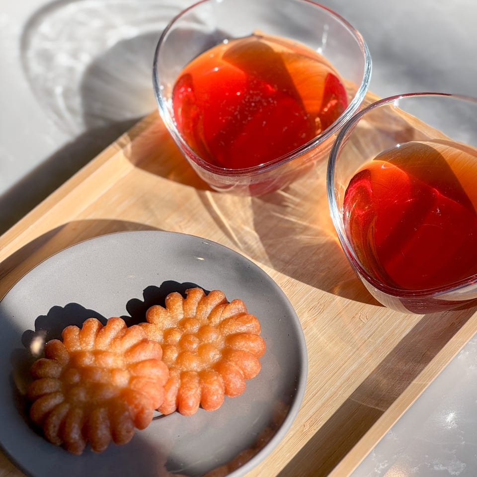 Two Korean yakgwa cookies on a grey plate next to two glasses of red sujeonggwa punch.