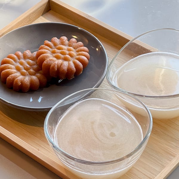 Two Korean yakgwa cookies on a gray plate with two bowls of sikhye on a wooden tray.